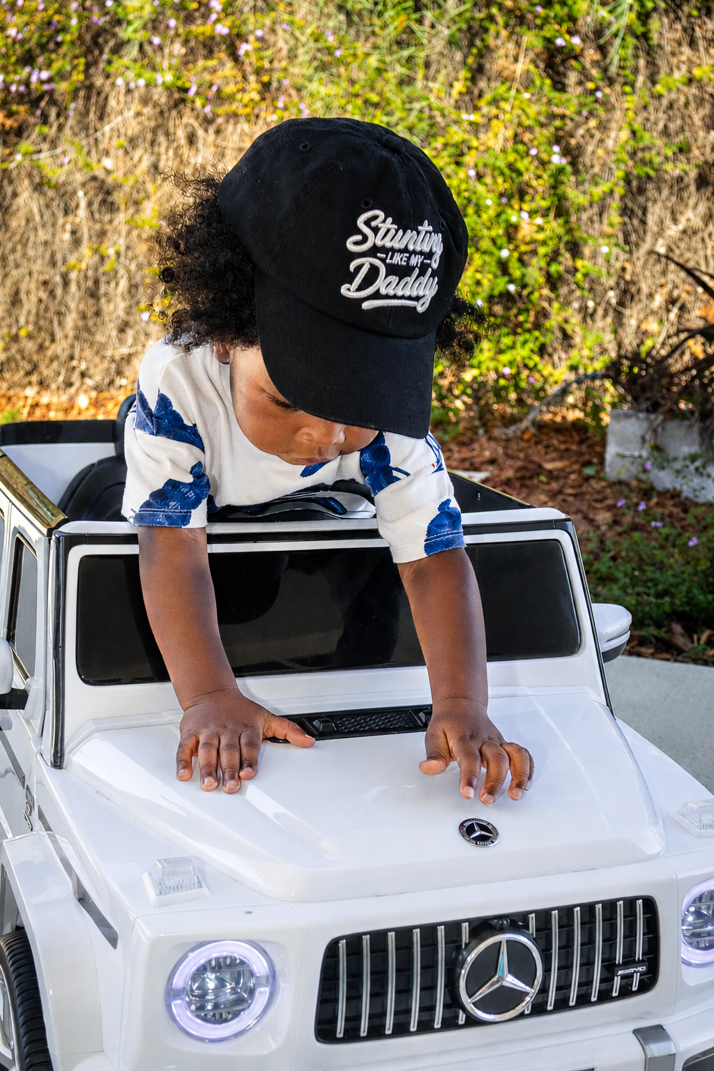 A child leaning across a white toy SUV in their black hat